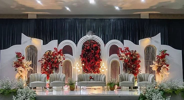 White arched stage with red floral displays and grey velvet seating